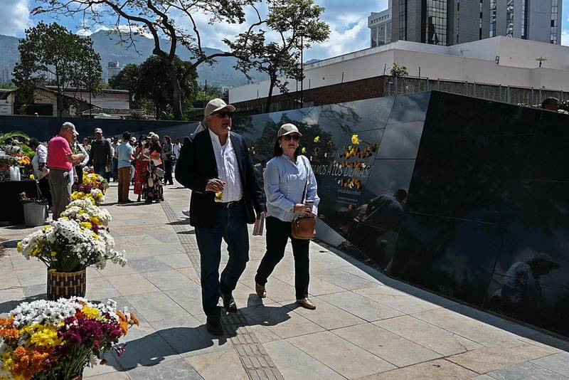 People walk next to a wall memorial in tribute to the victims of late Colombian drug lord Pablo Escobar, after the inauguration of the 'Inflection Park' in Medellin, on December 20, 2019. - The park was build on the same ground of the demolished Monaco building, which was once home to Escobar. (Photo by JOAQUIN SARMIENTO / AFP)