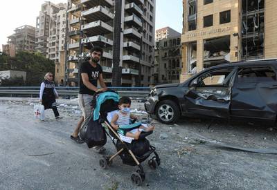 A man pushes a buggy with a child on Wednesday past a damaged vehicle near the scene of overnight blast in Beirut's port area. Reuters