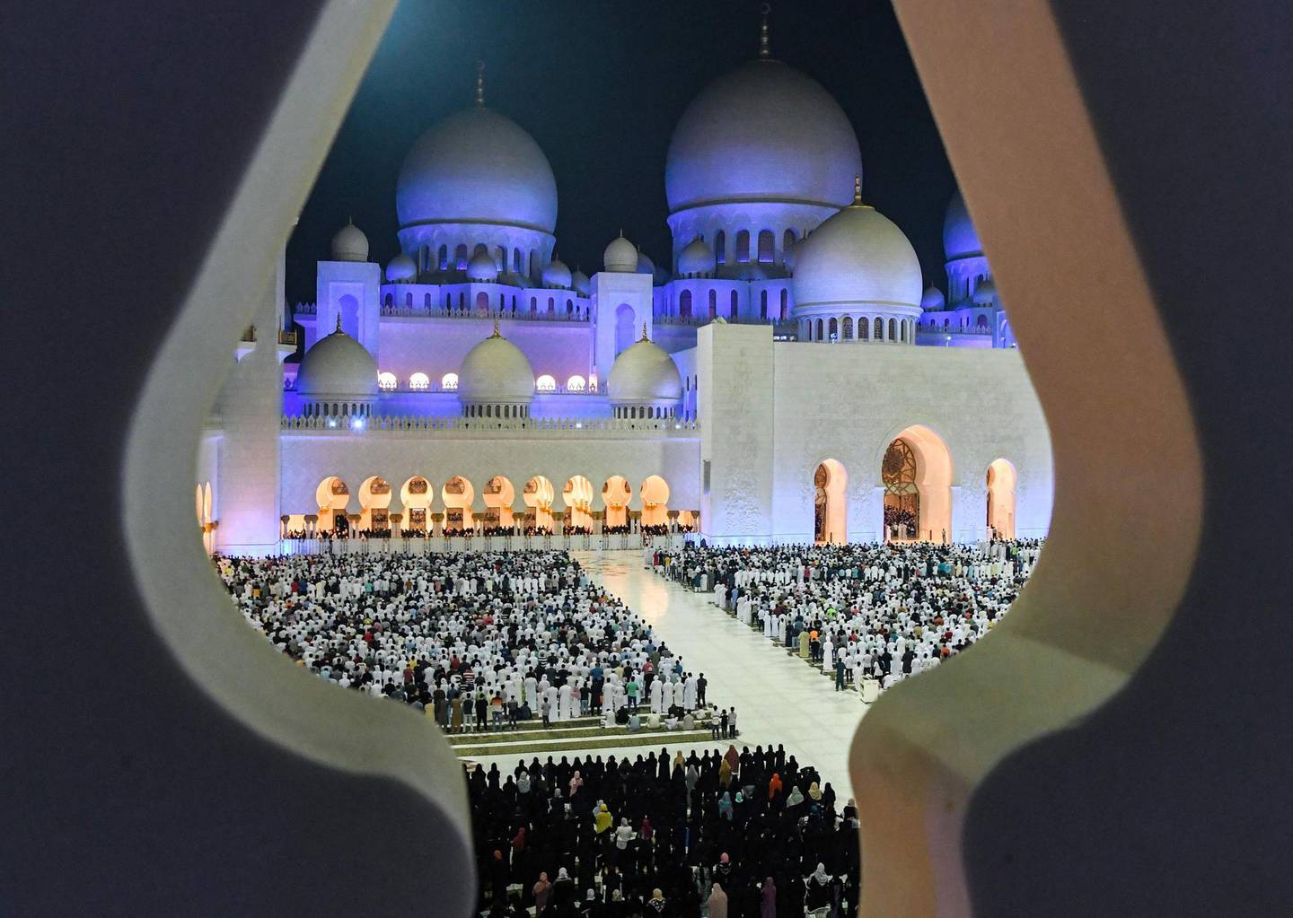 This picture taken early on June 1, 2019 through the crenellations of the Sheikh Zayed Grand Mosque in the UAE capital Abu Dhabi shows Muslim worshippers praying in the mosque's courtyard on the occasion of Lailat al-Qadr, which marks the night in the fasting month of Ramadan during which the Koran was first revealed to Prophet Mohammed in the seventh century.  / AFP / KARIM SAHIB
