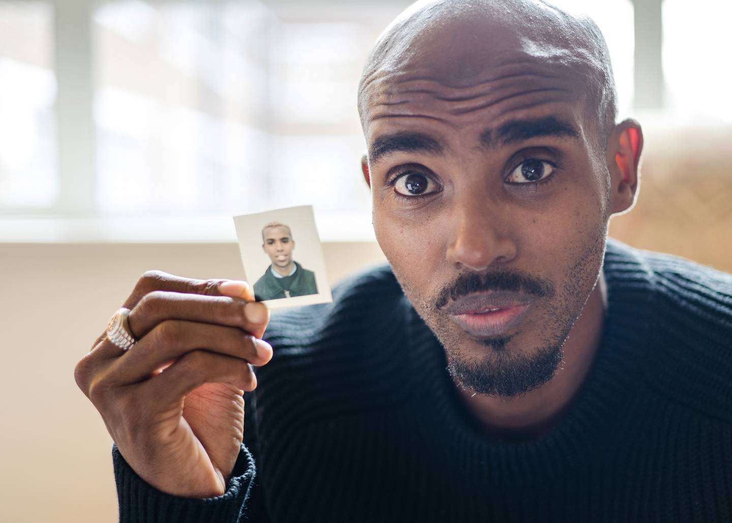 Sir Mo Farah holds a picture of himself as a child during the filming of the BBC documentary, 'The Real Mo Farah'. BBC / PA