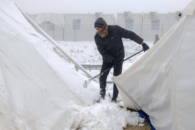 A migrant clears snow from makeshift tents. AP Photo