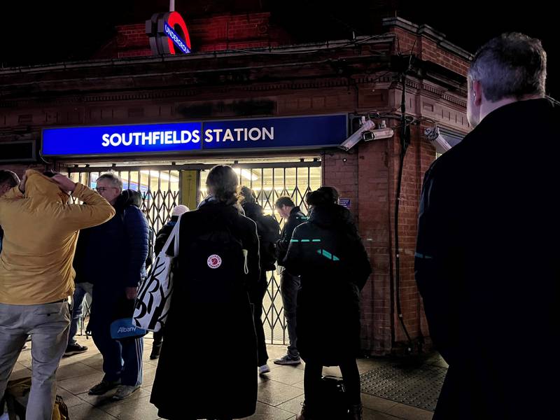 Passengers outside the locked gates of Southfields London Underground station, waiting for the first train of the day. PA