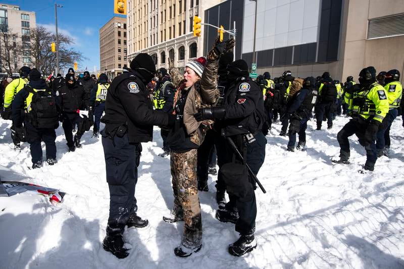 A protester sings 'O Canada' as she is arrested after trying to push through a line of police officers. AP