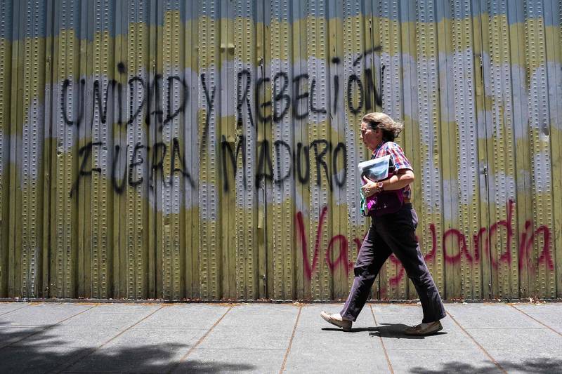 A woman walks past a graffiti reading "Unity and rebellion, out Maduro" in Caracas, on May 2, 2019. AFP