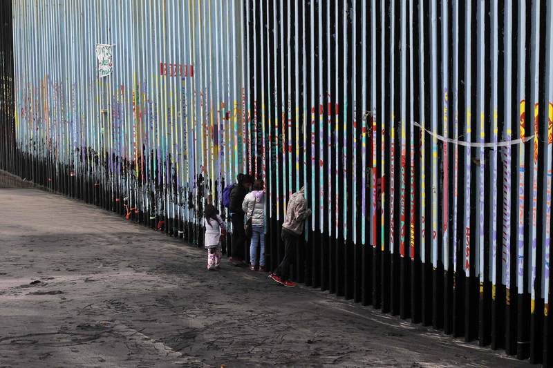 A family of Central American migrants look through the US-Mexico border fence, as seen from Playas de Tijuana. AFP
