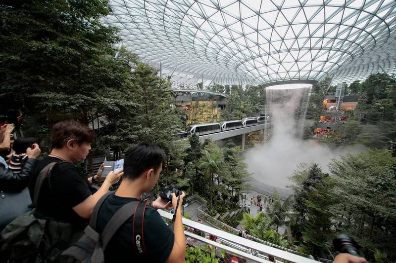 epa07498505 Members of the public take photographs of the Rain Vortex inside Jewel Changi in Singapore, 11 April 2019.Built at a cost of 1.7 billion SGD (just over 1 million euro), the Jewel is a hub that links Changi Airport's Terminals 1, 2, and 3. The ten-storey structure covers a 3.85 hectare area and includes a hotel, retail and dining outlets, early check-in counters and baggage areas. The central feature of Jewel Changi is the 40-metre Rain Vortex, the world's tallest indoor waterfall and the lush greenery that surrounds it.  EPA/WALLACE WOON
