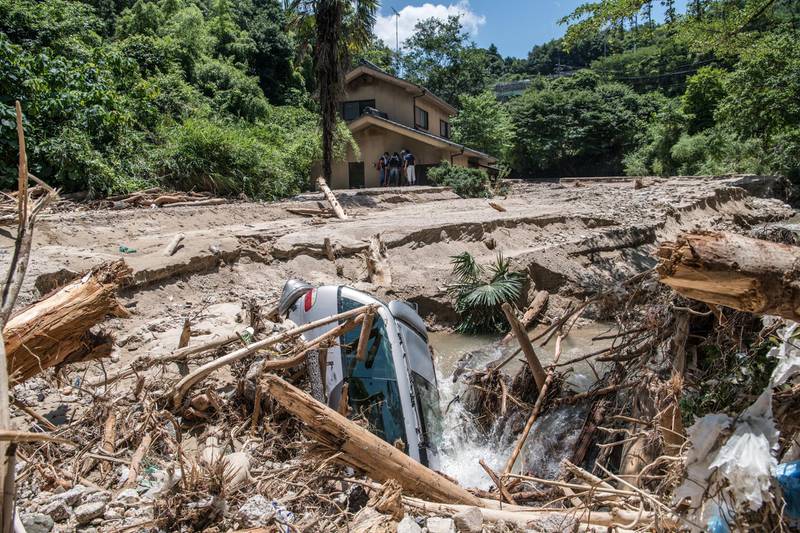 HIROSHIMA, JAPAN - JULY 10: A car lies in mud as people rest in the shade of a house that is partially submerged as they search for missing relatives following a landslide, on July 10, 2018 in Yanohigashi near Hiroshima, Japan. Over 112 people have died and 78 are missing following floods and landslides triggered by "historic" levels of heavy rain across central and western parts of Japan while more than 73,000 rescuers are racing to find survivors as temperatures rise. Japan's Prime Minister Shinzo Abe warned on Sunday of a "race against time" to rescue flood victims as almost 2 million people are subject to evacuation orders and tens of thousands remain without electricity and water. (Photo by Carl Court/Getty Images)