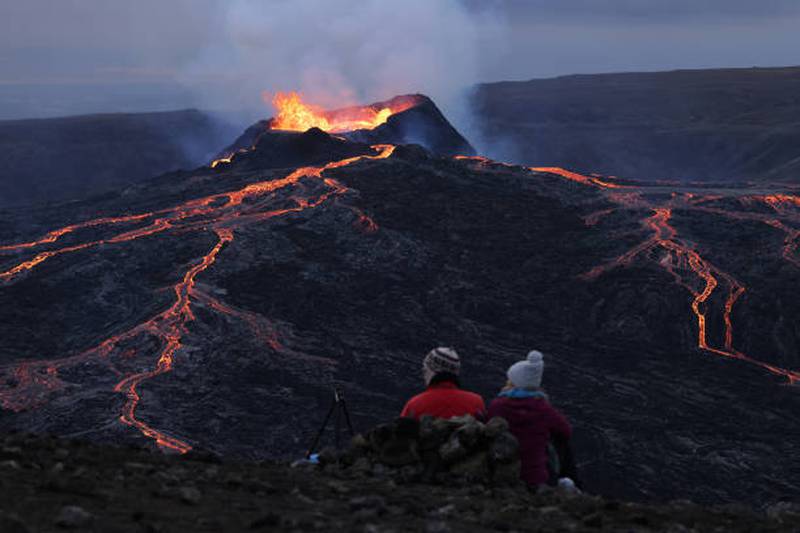 A couple sitting on a hill watch as the Fargradalsfjall volcano spews molten lava.  Getty Images