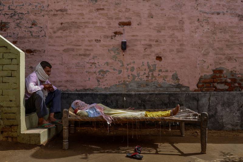 A man sits next to his wife as she receives rehydration fluid at a makeshift clinic during a surge of the coronavirus disease in Parsaul village, in the state of Uttar Pradesh, India, on May 22, 2021. By Adnan Abidi, Pulitzer Prize Winner for Feature Photography.  Reuters