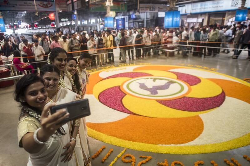 MUMBAI, INDIA - SEPTEMBER 4: A group of girls in traditional saree takes selfie in front of a huge rangoli made by flower petals on the occasion of Onam at CST station on September 4, 2017 in Mumbai, India. Onam is an annual harvest festival of Kerala. The festival is mainly celebrated by Malayalees around the world with traditional folk dances, artworks, etc. According to the Onam story and its popular myth, Lord Vishnu in his Vamana avtar sents King Mahabali to hell as the gods becomes jealous of his popularity. But grants him a boon that the king can visit his subjects once in a year. Thus, it is believed that Onam is celebrated as King Mahabali's visit to the place. It is the only festival in which both the winner and the defeater are worshipped. Onam Festival falls during the Malayali month of Chingam (Aug - Sep) and marks the homecoming of legendary King Mahabali. Carnival of Onam lasts for ten days and brings out the best of Kerala culture and tradition. (Photo by Pratik Chorge/Hindustan Times via Getty Images)