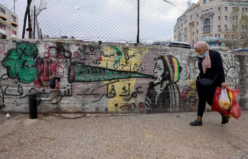 A Palestinian woman carries shopping bags as she walks past a graffiti-filled wall in the city center of Ramallah in the West Bank, on March 30, 2021.  / AFP / Emmanuel DUNAND
