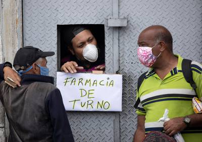 A man attends customers through an opening from which hangs a handwritten sign that reads in Spanish: "Pharmacy on duty," in Caracas, Venezuela. AP Photo