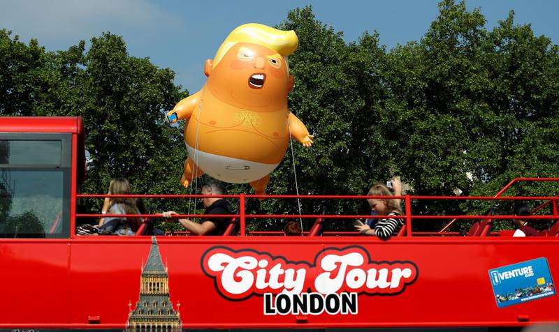 Demonstrators float the Trump blimp behind a red tourist bus. Rueters