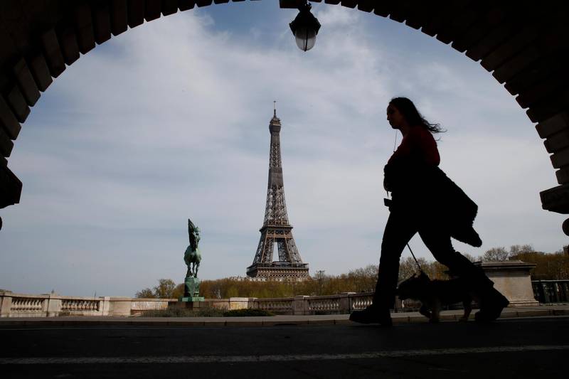 FILE - In this Tuesday, April 7, 2020 file photo, a woman walks her dog on a Paris bridge, with the Eiffel tower in background, during a nationwide confinement to counter the COVID-19. The European Union announced Tuesday, June 30, 2020 that it will reopen its borders to travelers from 14 countries, but most Americans have been refused entry for at least another two weeks due to soaring coronavirus infections in the U.S. (AP Photo/Christophe Ena, File)