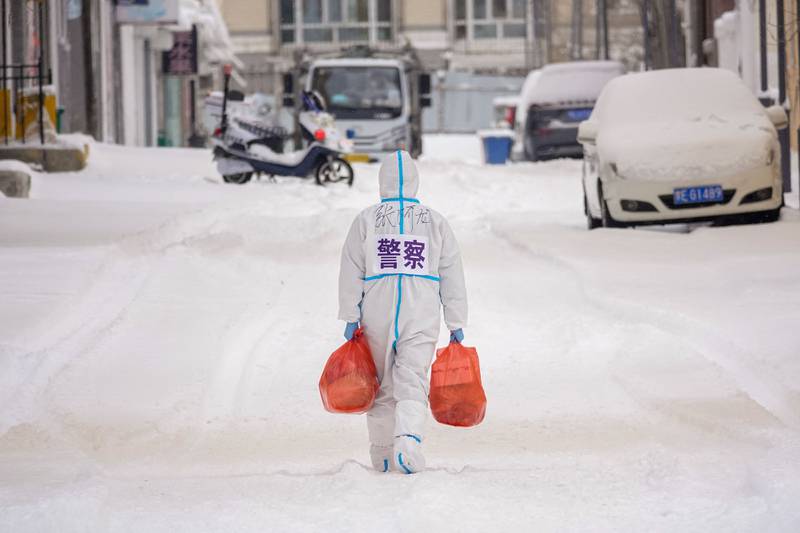 A police officer in personal protective equipment carries supplies to be distributed to residents at a residential area restricted because of the spread of the Covid-19 coronavirus in Manzhouli in China's northern Inner Mongolia region on March 15, 2022. AFP