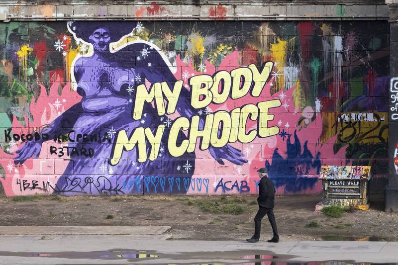 A man walks along the bank of the Danube Canal during the lockdown in Vienna. Graffiti on the wall reflects opposition to the Covid-19 vaccination campaign. AP