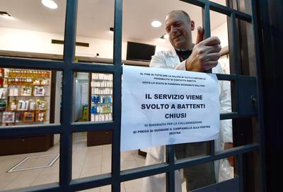 A pharmacist approaches the entrance gate of the drugstore during the national coronavirus emergency lockdown, in Genoa. EPA