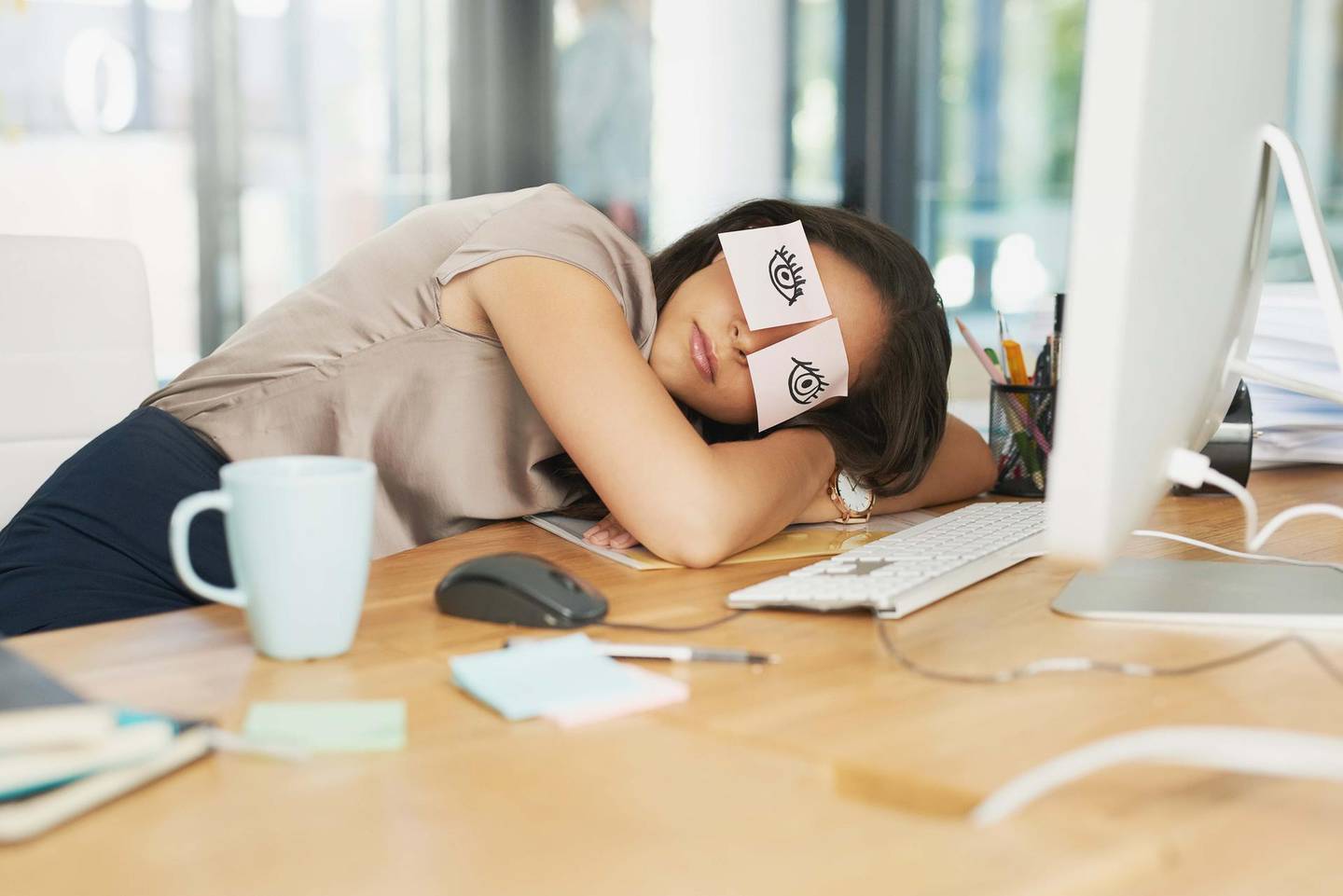 Shot of a tired businesswoman napping at her desk with adhesive notes on her eyes. Getty Images