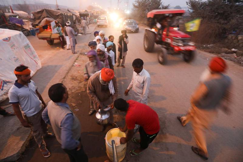 Farmers stand in a line to fill vessels with milk at the site of a protest against newly passed farm bills at Tikri border near Delhi, India, December 11, 2020. REUTERS/Anushree Fadnavis