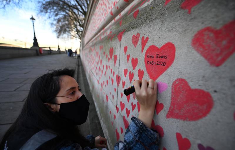 A volunteer paints hearts on the wall along the embankment opposite parliament as part of the National Covid Memorial Wall in London. EPA