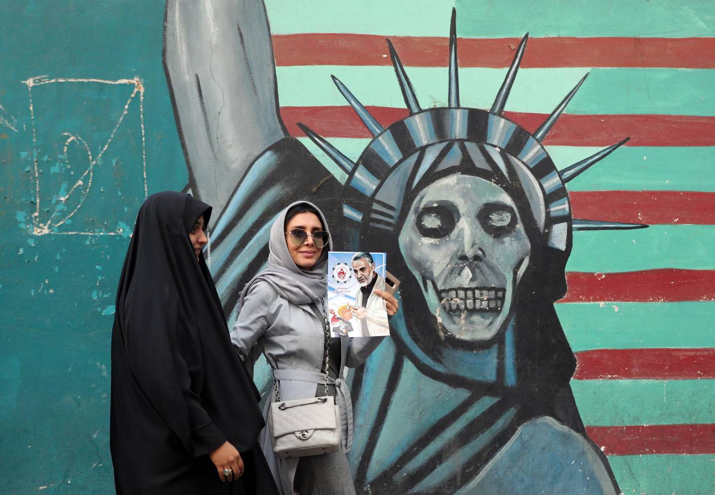 epaselect epa07140552 An Iranian woman (C) holds a poster of Iranian Major General in the Islamic Revolutionary Guard Corps (IRGC) Qasem Soleimani as she walks past a mural depicting a skull-faced Statue of Liberty during an anti-US demonstration marking the 39th anniversary of US Embassy takeover, near the former US embassy in Tehran, Iran, 04 November 2018. Media reported that thousands of protesters chanting 'Death to America' gathered at the former US embassy in Tehran to mark the 39th anniversary of the start of the Iran hostage crisis. Iranian students occupied the embassy on 04 November 1979 after the USA granted permission to the late Iranian Shah to be hospitalized in the States. Over 50 US diplomats and guards were held hostage by students for 444 days. US President Donald J. Trump's administration announced on 02 November 2018, that it will reimpose sanctions against Iran that had been waived under the 2015 Iran nuclear deal (the Joint Comprehensive Plan of Action, JCPOA). The US sanctions will take effect on 05 November 2018, covering Iran's shipping, financial and energy sectors. In 2015, five nations, including the United States, worked out a deal with the Middle Eastern country that withdrew the sanctions, one of former US President Barack Obama's biggest diplomatic achievements.  EPA/ABEDIN TAHERKENAREH
