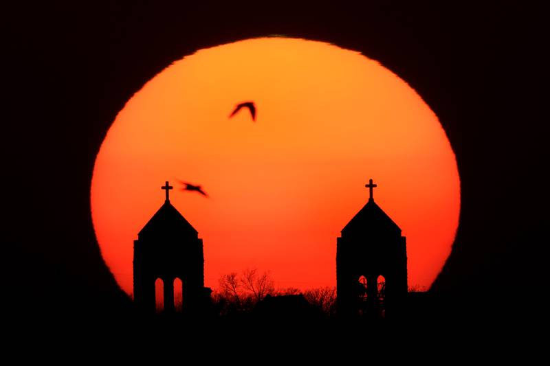 Birds fly past the twin steeples of the Hosanna Karen Baptist church as the sun sets in Kansas City. AP
