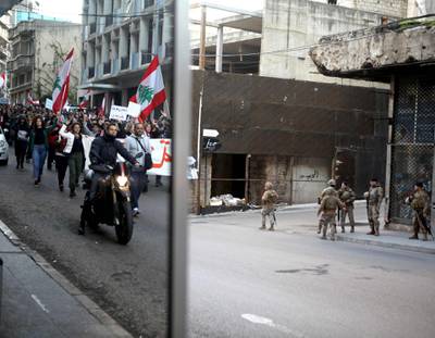 An image reflected in a shop window shows Lebanese anti-government protesters marching down a road on Beirut’s civil war demarcation line between the city's east and west as army soldiers look on from across the road. AFP