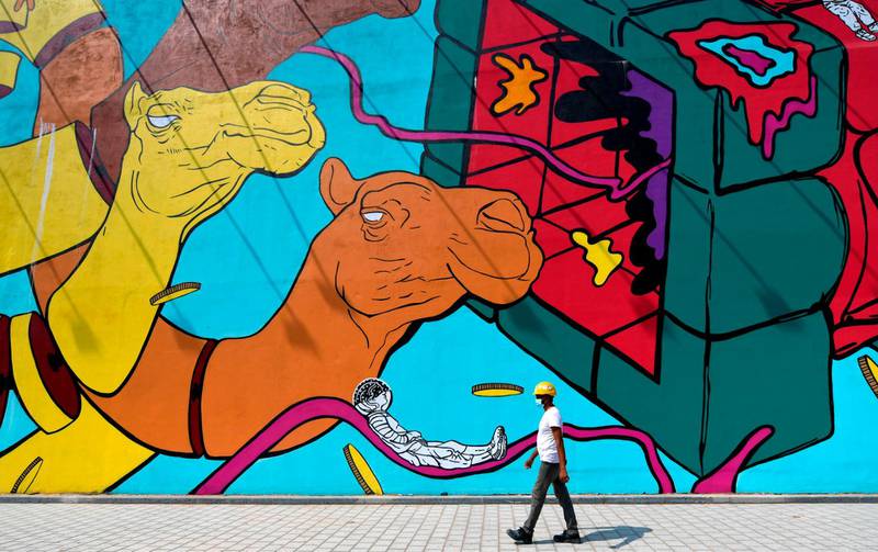 A worker wearing a hard hat walks past a mural in Dubai. Shopping malls in Dubai fully reopened for business on June 3.  AFP