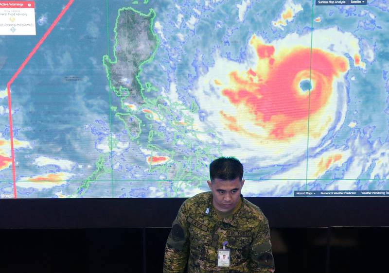 A member of the Philippine Air Force stands in front of a satellite image of Typhoon Mangkhut, locally named Typhoon Ompong, at the National Disaster Risk Reduction and Management Council operations center in metropolitan Manila, Philippines on Thursday, Sept. 13, 2018. Philippine officials have begun evacuating thousands of people in the path of the most powerful typhoon this year, closing schools and readying bulldozers for landslides. (AP Photo/Aaron Favila)