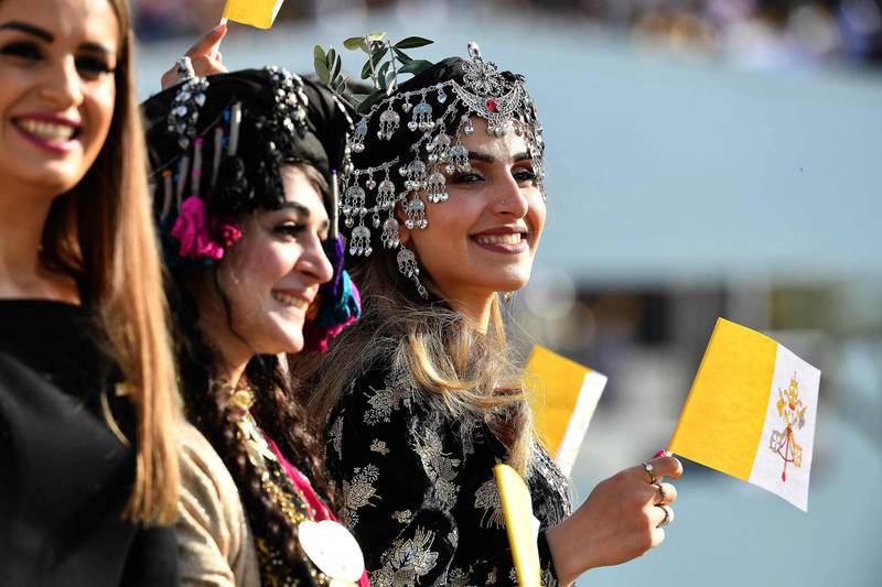 Young women dressed in traditional Kurdish clothing wave flags of the Holy See as they wait for the arrival of Pope Francis at the Franso Hariri Stadium in Erbil. AFP