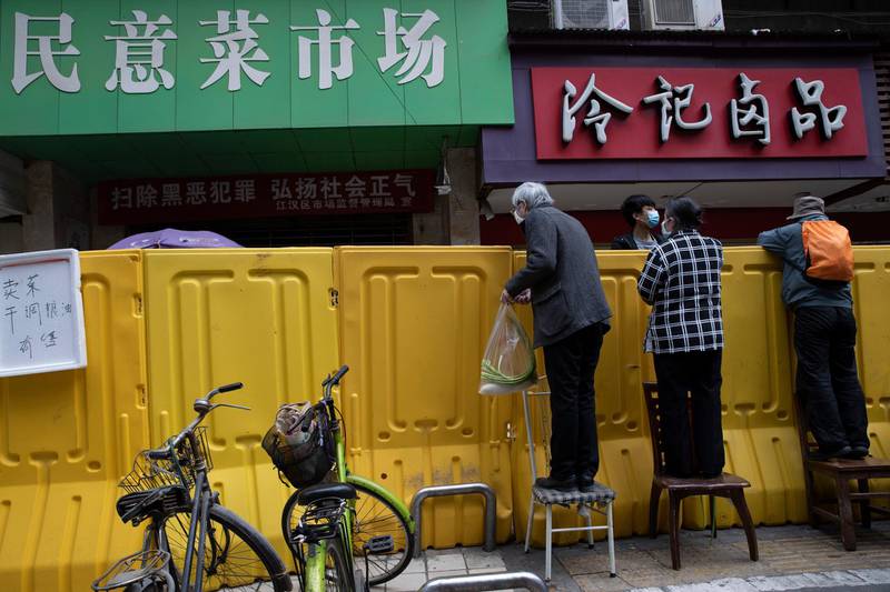 Residents climb on chairs to buy groceries from vendors behind barriers used to seal off a neighborhood in Wuhan in central China's Hubei province. AP Photo