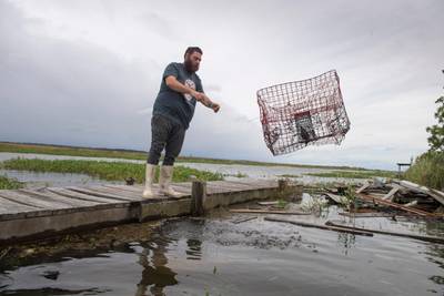 Casey Guidry tosses one of several crab traps that had been pushed around from the rising water near his home along Salt Bayou near Slidell, Louisiana. AP