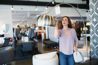 Woman checking price tag on lamp in home furnishings store. Getty Images