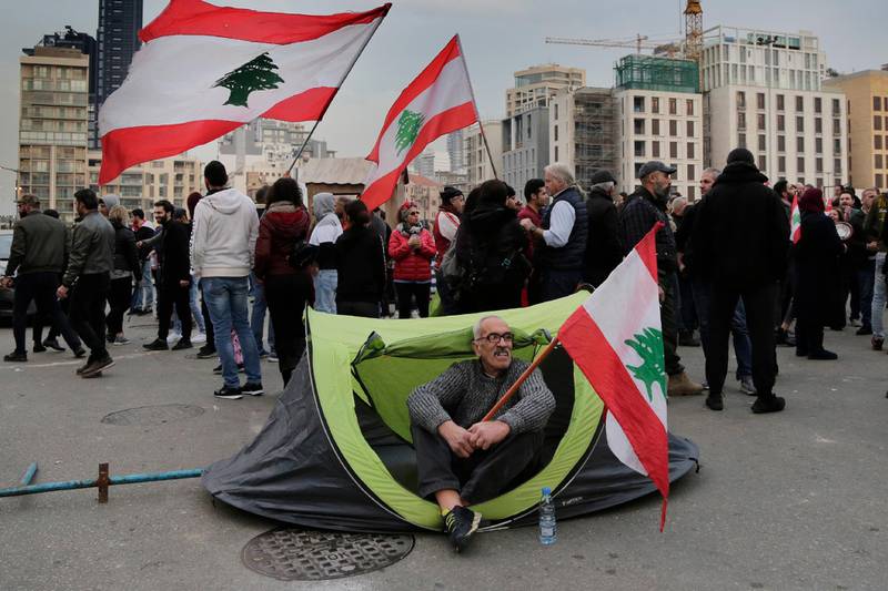An anti-government protester sits inside a tent as others block a road that links to the Martyrs square where they set their protest encampment, after it was opened by the security forces in the morning, in downtown Beirut, Lebanon, Tuesday, Jan. 28, 2020. (AP Photo/Hassan Ammar)