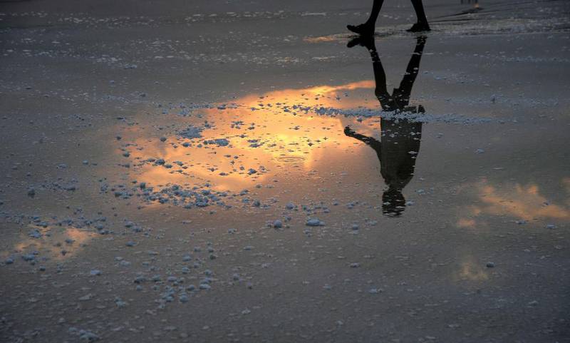 An Indian labourer and the rising sun are reflected in water as arrives to work on a salt pan on the outskirts of Mumbai. Vast tracts of over 3,000 acres of “salt pan” lands in Mumbai might disappear soon as a proposal to convert them to housing projects for displaced squatters is in the offing. Indranil Mukherjee / AFP