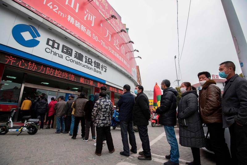 This photo taken on February 25, 2020 shows customers lining up to have their temperature taken before entering the bank in Nantong, in China's eastern Jiangsu province. The bank was controlling the number of people inside the bank at any one time as a precaution against the COVID-19 coronavirus. China on February 26 reported 52 new coronavirus deaths, the lowest figure in more than three weeks, bringing the death toll to 2,715. - China OUT
 / AFP / STR
