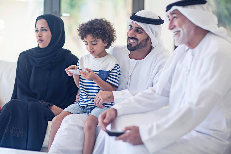 Middle Eastern family watching television, family is enjoying watching a TV Series while the kid is playing with the mobile phone.