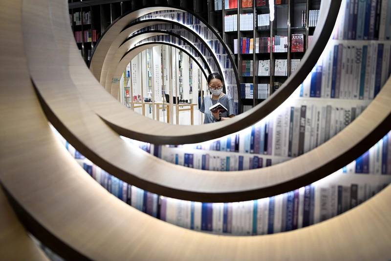 A woman wearing a face mask picks up a book at a bookstore in Beijing.   AFP