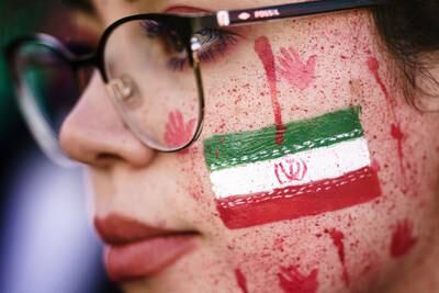 A protester shows red paint on her face, resembling blood splatters and bloody handprints next to the national Iranian emblem, during a rally in Berlin. EPA