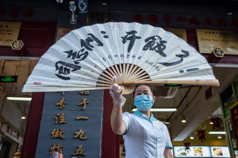 epa08444685 A waitress wearing a protective face mask holds a folding fan reading 'comrades, time for meal' outside a restaurant in Beijing, China, 26 May 2020.  EPA/WU HONG