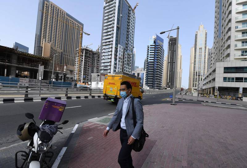 A man, wearing a protective mask, walks down the street in Dubai on March 16, 2020. No shisha pipe sessions, deserted streets, mosques and shopping malls, drones in the sky broadcasting public health warnings -- the new coronavirus has turned life upside down in Gulf societies. / AFP / KARIM SAHIB
