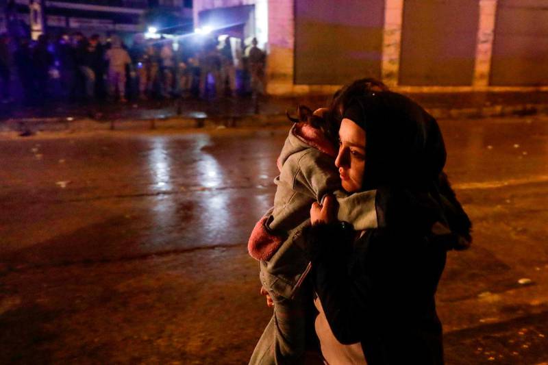 A woman crosses a street with her child during clashes between security forces and anti-government protesters in the northern city of Tripoli, on January 29, 2021. AFP
