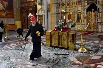 An Orthodox priest clears up glass and debris inside the Holy Intercession Cathedral. It was damaged in missile strikes from Russian forces.  AFP