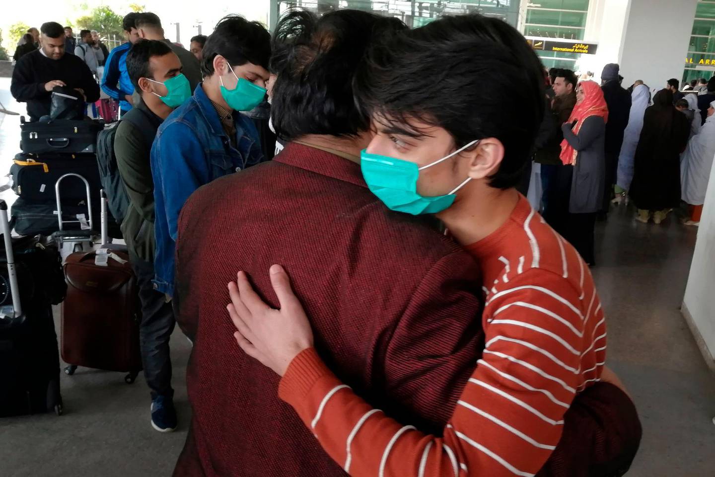A Pakistani student wearing protective facemask hugs with a relative upon his arrival with other students from China at the Islamabad International Airport in Islamabad on February 3, 2020. Pakistan on February 3 resumed flight operations with China, days after it had suspended all direct flights with China as the death toll from the coronavirus epidemic soared past 360. The China Southern Airlines' flight from China brought 69 passengers including 57 Pakistanis and 12 Chinese to Islamabad International Airport, according to Zafar Mirza, special assistant to Prime Minister Imran Khan on heath. / AFP / Aamir QURESHI
