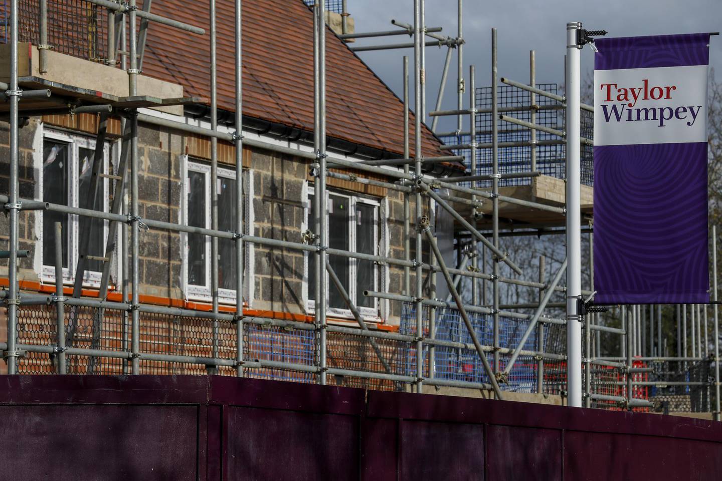 A sign bearing the Taylor Wimpey Plc logo stands near scaffolding surround a new housing development at Worplesdon, near Guildford, U.K., on Wednesday, Nov. 20, 2019. The U.K. still suffers from an imbalance between the demand for housing and the volume of new houses being built, so any party campaigning for government would likely have to address this as part of their policy platform. Photographer: Luke MacGregor/Bloomberg