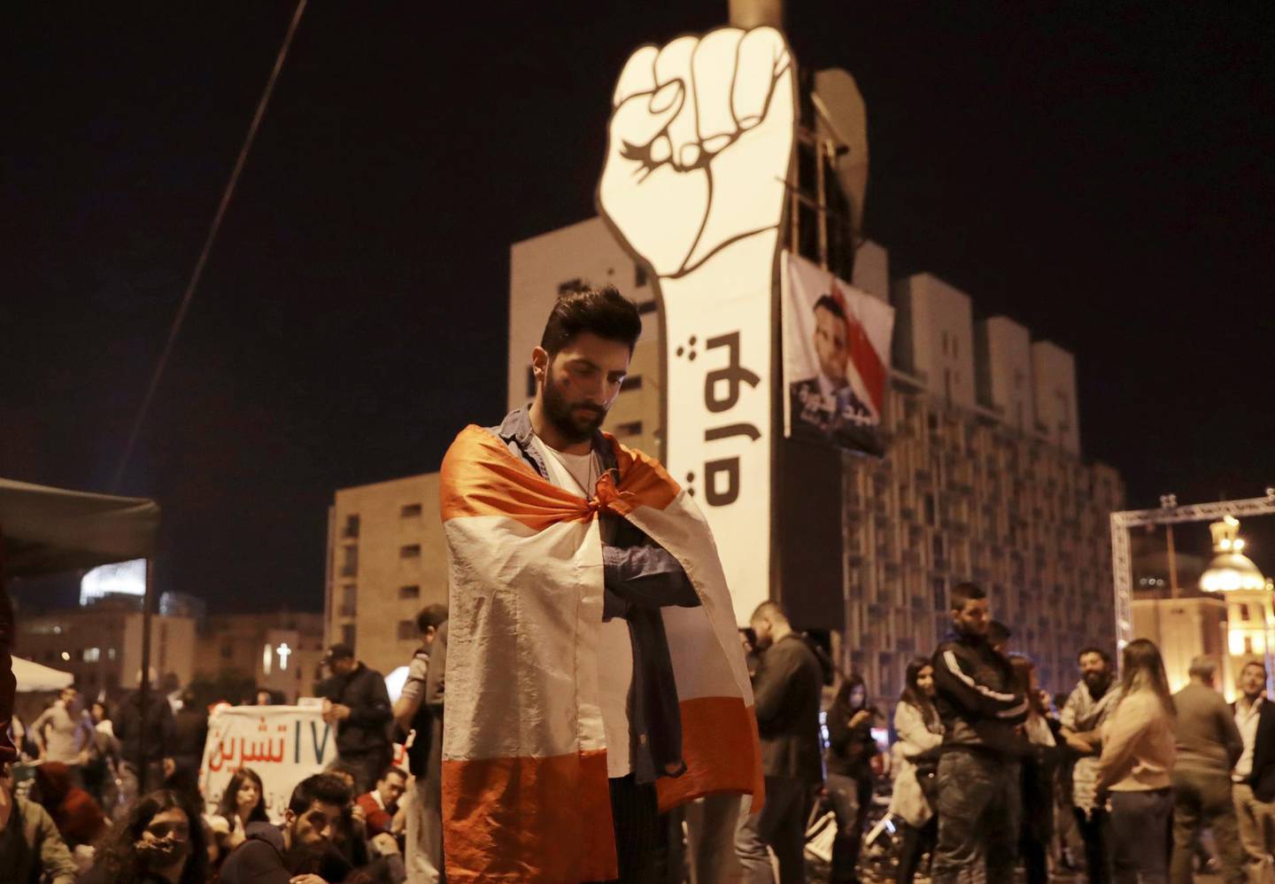 Anti-government protesters listen to the Lebanese President Michel Aoun as he delivers a televised speech on the eve of the country's 76th Independence Day, in downtown Beirut, Lebanon, Thursday, Nov. 21, 2019.  Aoun barely mentioned the month-long protests in his speech and said consensus on government formation remained far off because of "contradictions that control Lebanese politics." He didn't elaborate. (AP Photo/Hassan Ammar)