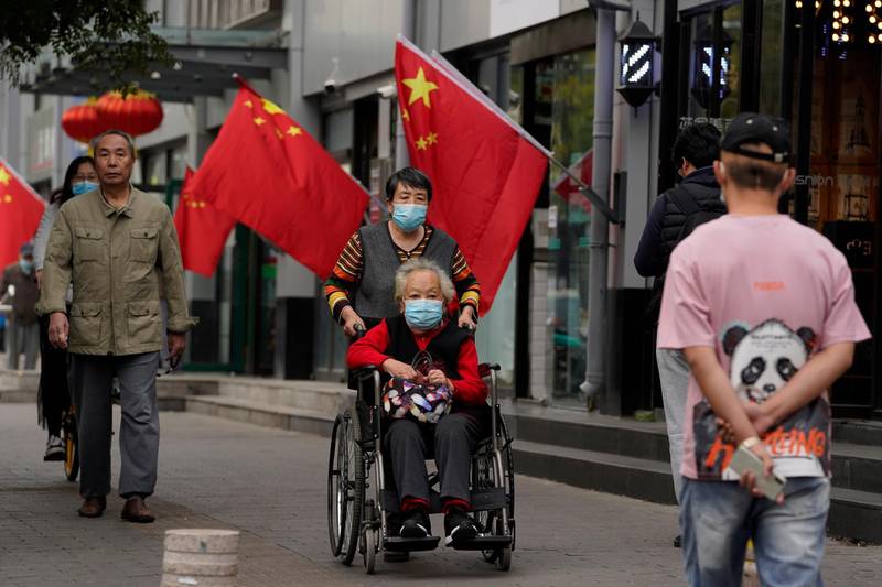 An elderly woman is wheeled past national flags on the last day of the National Day holidays in Beijing, October 8, 2020. Ng Han Guan / AP