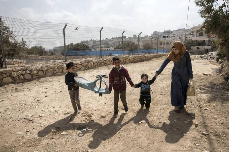 A Palestinian woman with children pass by the fence of the new archeological park that the Israeli government and army Palestinian neighbourhood of Tel Rumeida in Hebron .(Photo by Heidi Levine for The National).