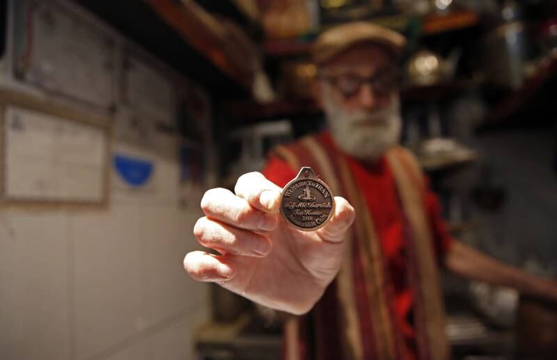 Mr Mabhutian holds a metal coin inscribed with a poem along with the name of his Haj Ali Darvish Teahouse.