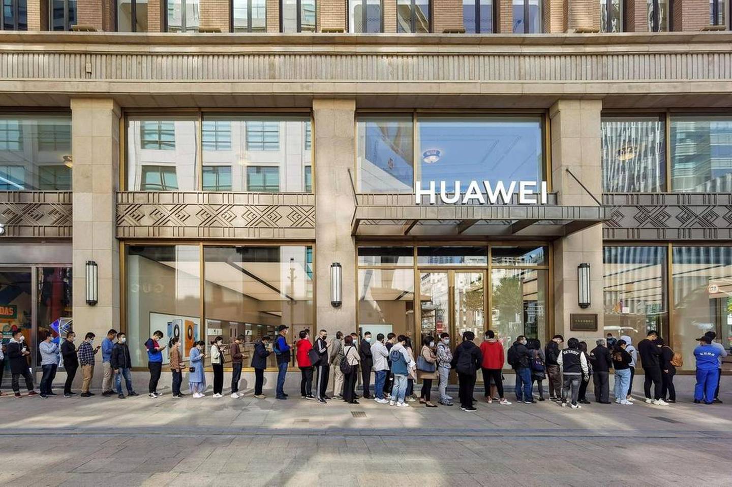 People wearing masks wait in line in front of the Huawei’s flagship store for pre-sales of the Huawei Mate 40 series smartphones, launched in October, in Shanghai. AFP